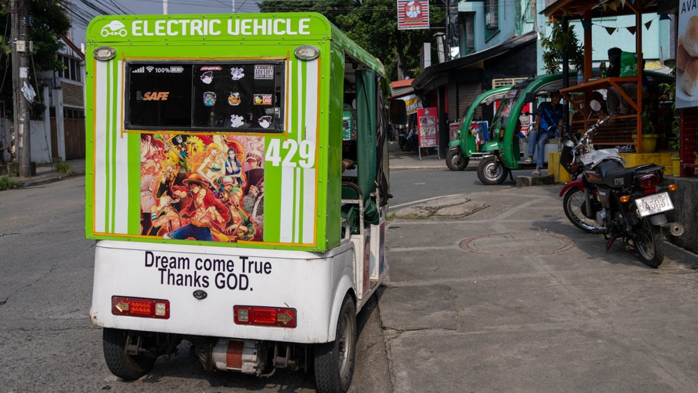 The back of an three wheeler with text stickers reading 'Electric Vehicle' and 'Dream come True Thanks GOD'.